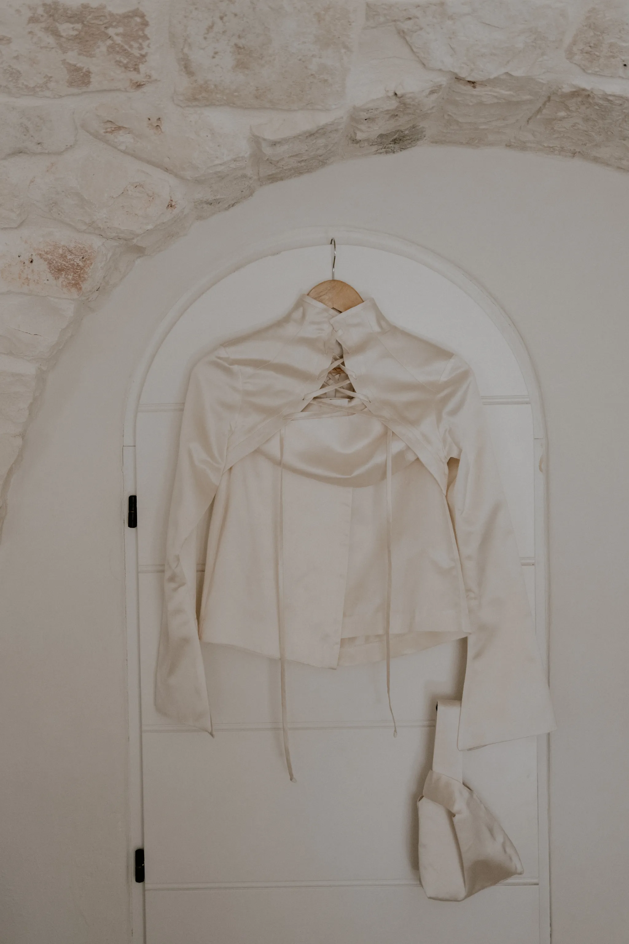Abito da sposa bianco appeso a una porta ad arco in pietra in Puglia